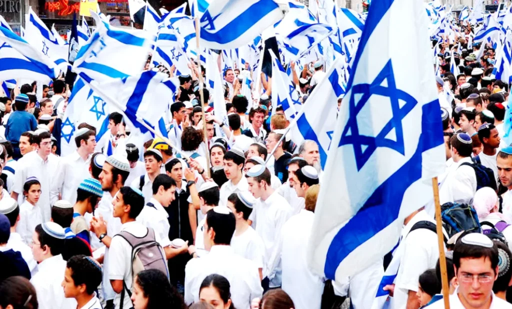 Crowd of people gathered outdoors waving Israeli flags during a public celebration or march.