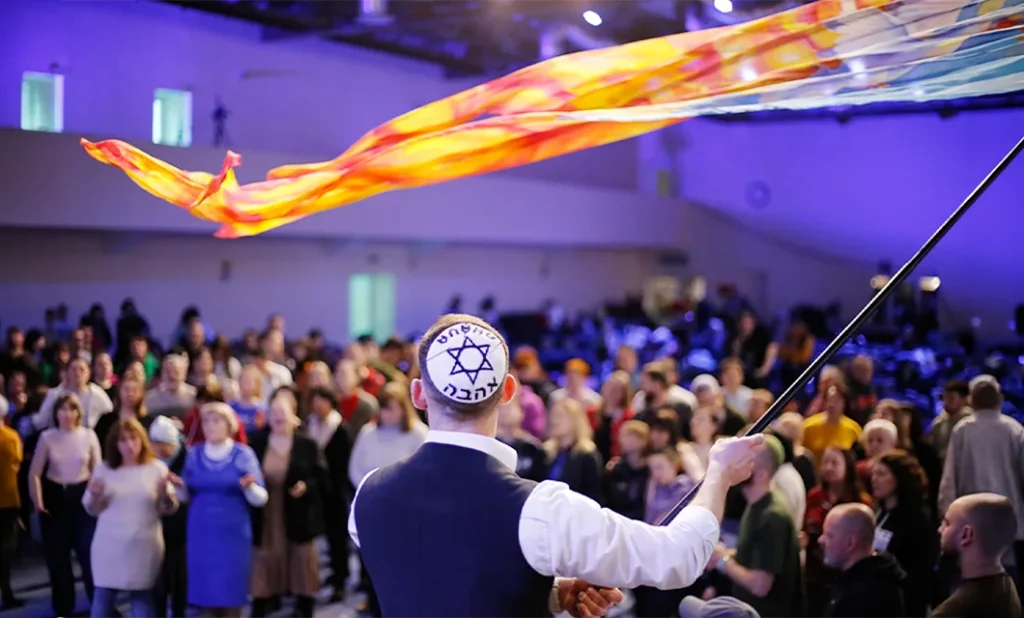 A man wearing a Star of David kippah waves a worship flag in front of a large Messianic congregation