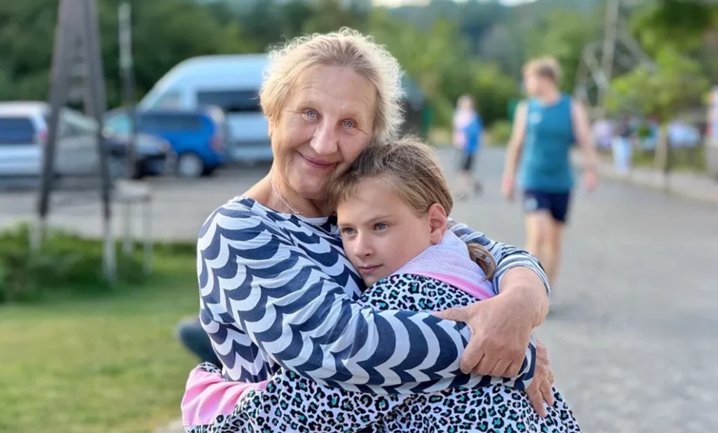 A caregiver embracing a young girl warmly outdoors at a children's camp in Ukraine