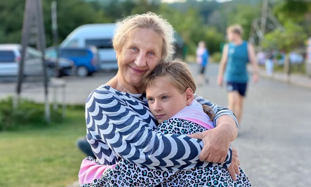 A caregiver embracing a young girl warmly outdoors at a children's camp in Ukraine