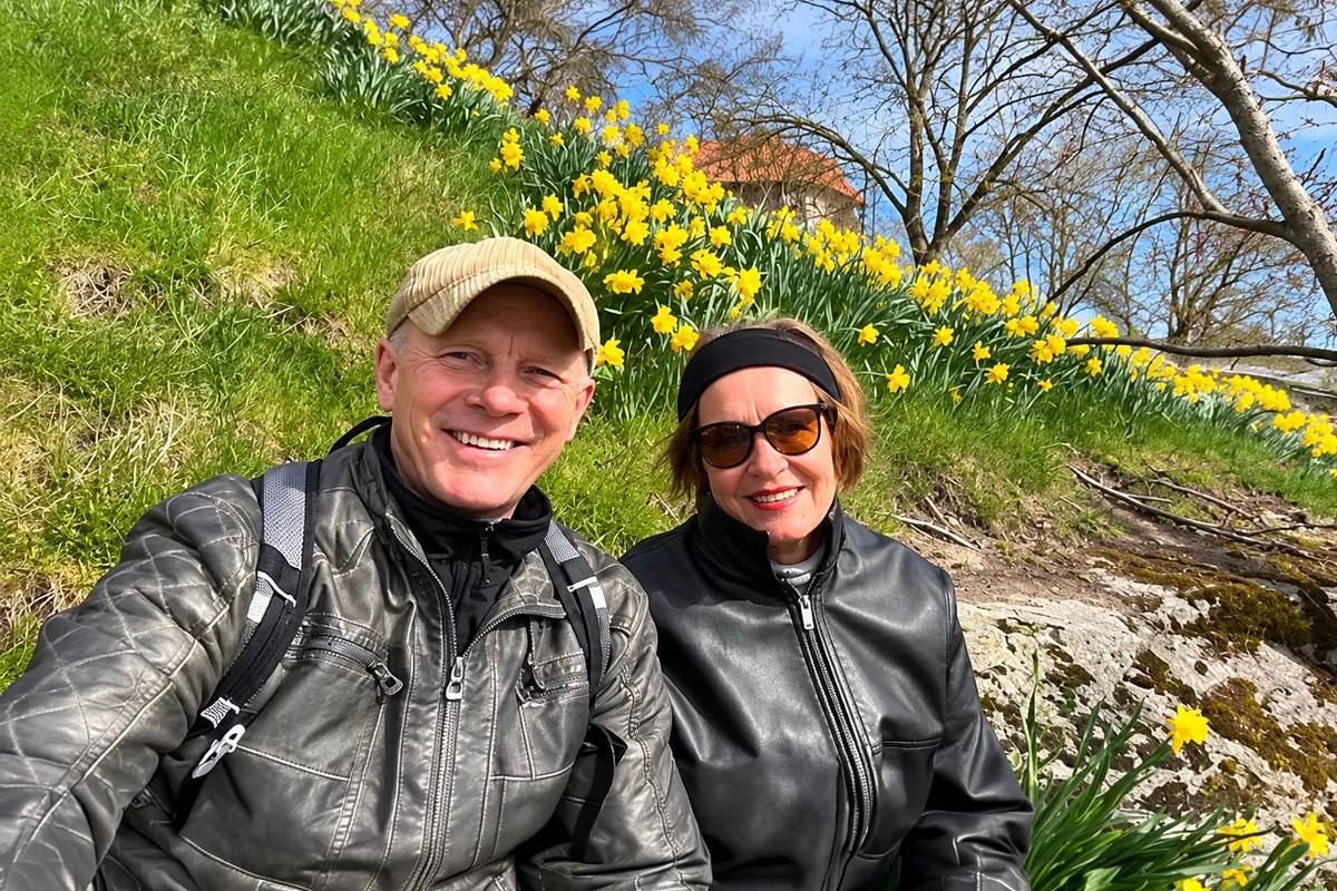 Vladimir and Pirjo Karttunen seated together outdoors with yellow flowers behind them.