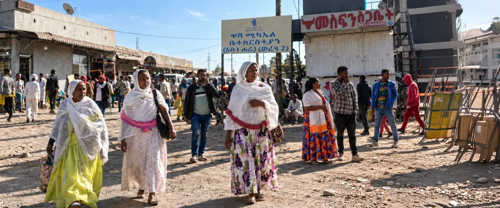 Three women wearing traditional white shawls walk along a busy street in Ethiopia, with pedestrians and shops in the background.