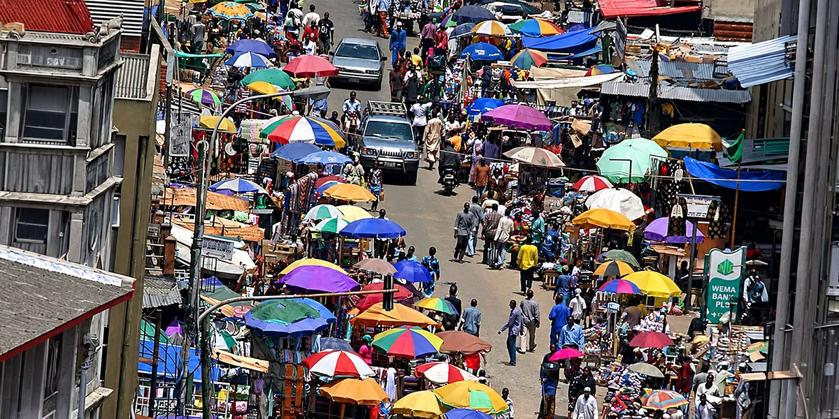Shoppers and vendors fill a busy Ethiopian street market, with colorful umbrellas covering stalls along the road.