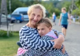 A caregiver embracing a young girl warmly outdoors at a children's camp in Ukraine